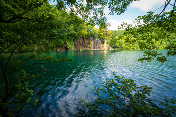 Obraz premium Cascades of pure fresh water rushing down brown, mossy rocks into an azure colored lake at the Plitvice Lakes National Park, Plitvička Jezera, Croatia