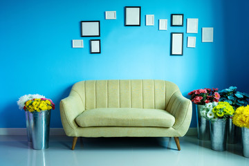 Vintage sofa with flower pots and photo frames on blue wall in living room.
