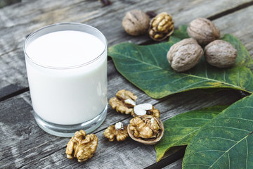 A glass of white milk and walnuts on an old wooden table. Vegan milk from walnuts. Eco food.