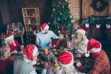 Top high angle photo of large family wear santa claus hat cap meeting on x-mas eve sit table eat talk speak among generation with small little boy girl mature pensioners in house have christmas tree
