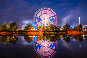 Germany, Illuminated colorful big wheel in motion and rollercoaster of popular folk festival called...