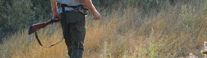 Hunting period, autumn season open. A hunter with a gun in his hands in hunting clothes in the autumn forest in search of a trophy. A man stands with weapons and hunting dogs tracking down the game.	