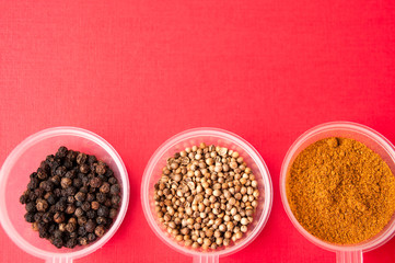 Spices: black pepper, ground red pepper and coriander peas in jars on a red background