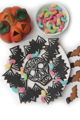Fototapeta na wymiar Halloween cookies in shape of a skull and bat with colorful worm candies on a plate isolated on white background. Halloween sweet food