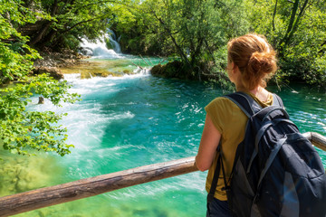 Woman watching pure water splashing down the natural barrier into an azure colored lake at the Plitvice Lakes National Park, Plitvička Jezera, Croatia