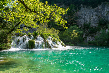 Fototapeta na wymiar Rushing water cascades down the natural barriers into the crystal clear and azure coloured Lake Gavanovac at the Plitvice Lakes National Park, Croatia