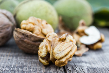 Walnut kernels and whole walnuts lie next to nuts in green shells and green leaves on a rustic old wooden table.