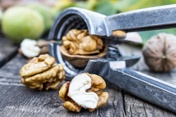 Walnuts and walnut kernels lie on a rustic old wooden table near the nutcracker. Kernels of walnuts.