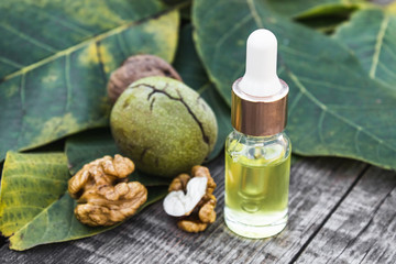 Walnut oil in a glass jar near walnuts and green leaves on a wooden table.