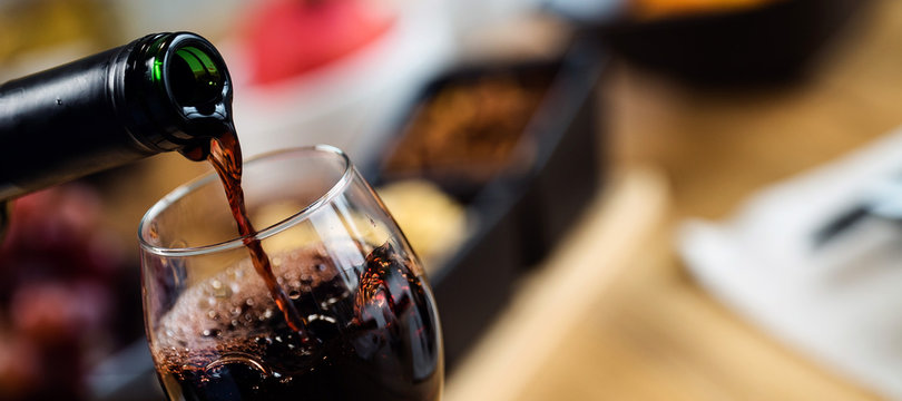 Red wine pouring into a wine glass at a tasting with various types of appetizers. 