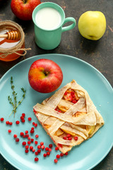 Apple pie with lingonberries and honey on a bright plate. Milk and apples on the table.