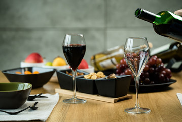 Red wine pouring into a wine glass at a tasting with various types of appetizers. 