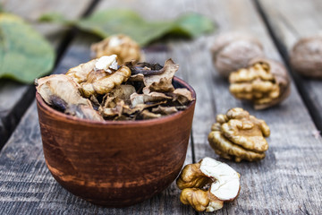Walnut kernels and partitions in a bowl and whole walnuts on a wooden table. A medicine for tinctures and decoctions.