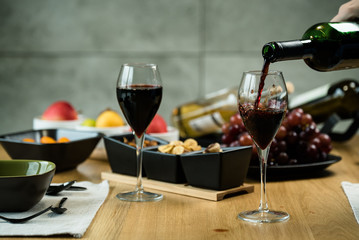 Red wine pouring into a wine glass at a tasting with various types of appetizers. 