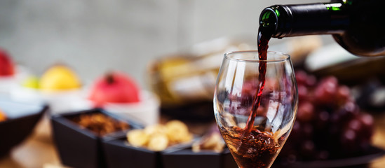 Red wine pouring into a wine glass at a tasting with various types of appetizers.  - 293964367