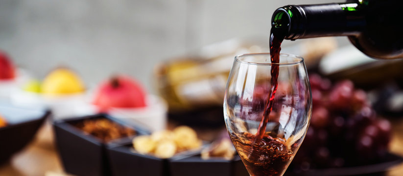 Red wine pouring into a wine glass at a tasting with various types of appetizers. 