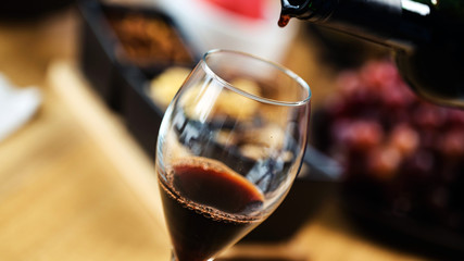 Red wine pouring into a wine glass at a tasting with various types of appetizers. 