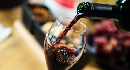 Red wine pouring into a wine glass at a tasting with various types of appetizers.  - 293964760