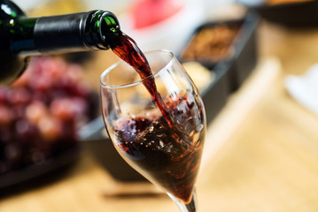 Red wine pouring into a wine glass at a tasting with various types of appetizers.  - 293964793
