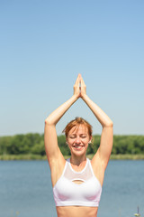 Fototapeta na wymiar Young girl practices yoga near the river on a clear sunny day