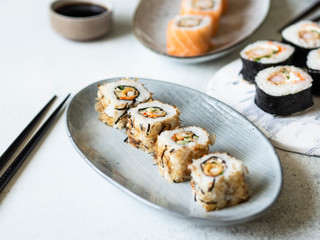 Variety of sushi rolls with shrimp, salmon, tuna served on ceramic plate and board.