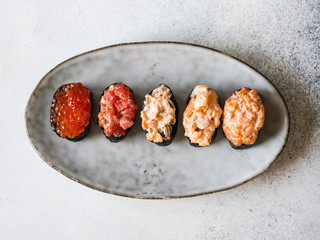 Variety gunkans with salmon, shrimp, tuna, mussels, red caviar on an oval ceramic plate. Top view