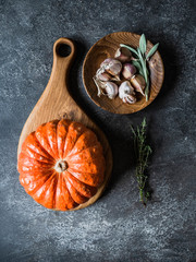 Fototapeta premium Ingredients for Making Autumn Seasonal Dishes - orange pumpkin, herbs, spices and garlic on dark grey background. Top view