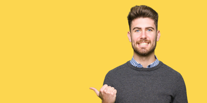 Young handsome elegant man smiling with happy face looking and pointing to the side with thumb up.