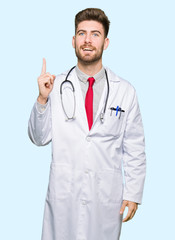 Young handsome doctor man wearing medical coat pointing finger up with successful idea. Exited and happy. Number one.