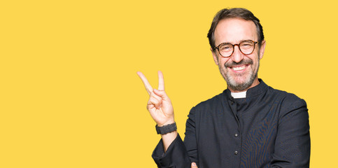 Middle age priest man wearing catholic robe smiling with happy face winking at the camera doing...