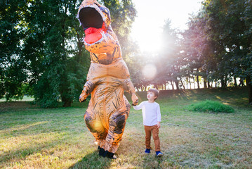 Father and son playing at the park, with a dinosaur costume, having fun with the family outdoor © oneinchpunch