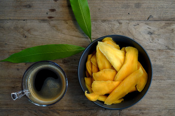 Dehydrated Mango or Dried Mango slices in navy bowl on wooden table   with coffee and mango leaf  