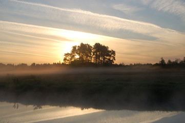 knoll Tumulus trees in the fog on the river. Summer sunrise. 