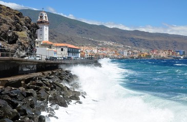 Ocean sea waves near black rocks. Church chapel and town with orange roofs. Tenerife Candelaria