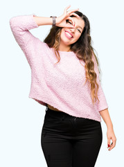 Young beautiful woman wearing pink sweater doing ok gesture with hand smiling, eye looking through fingers with happy face.