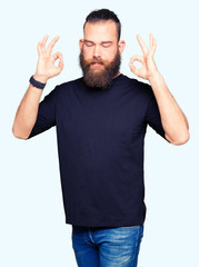 Fototapeta premium Young blond man wearing casual t-shirt relax and smiling with eyes closed doing meditation gesture with fingers. Yoga concept.