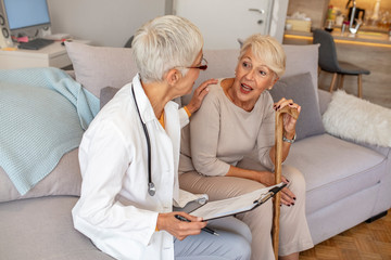 Obraz premium Senior woman is visited by her healthcare worker at home. Female doctor is consulting a senior patient. Smiling nurse sits with elder woman . Health visitor and a senior woman during home visit.