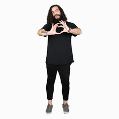Fototapeta premium Young man with long hair and beard wearing heavy metal black outfit smiling in love showing heart symbol and shape with hands. Romantic concept.