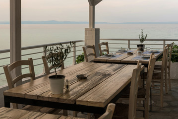 Mediterranean restaurant wooden table with Olive tree, dining setup, salt and pepper and sea view