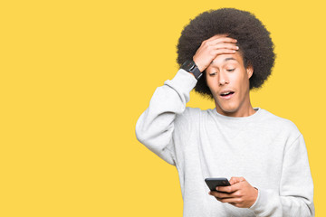 Young african american man with afro hair using a smartphone stressed with hand on head, shocked with shame and surprise face, angry and frustrated. Fear and upset for mistake.