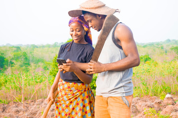 excited african couple doing internet banking on their farmland. male and female farmers using...
