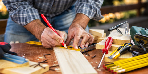 Adult carpenter craftsman with a pencil and the carpenter's square trace the cutting line on a wooden table. Construction industry, housework do it yourself. Stock photography.