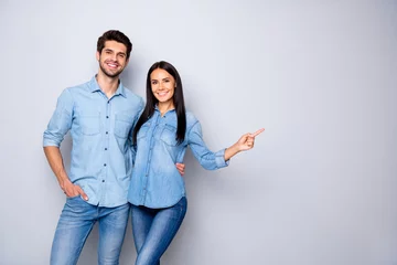 Fotobehang Photo of cheerful trendy charming brown haired nice cute couple of two people pointing at emptiness away wearing jeans denim jackets isolated over grey color white background © deagreez