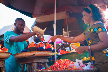 Black girl choosing tomatoes from a local market seller. man selling tomatoes to a young woman - obrazy, fototapety, plakaty
