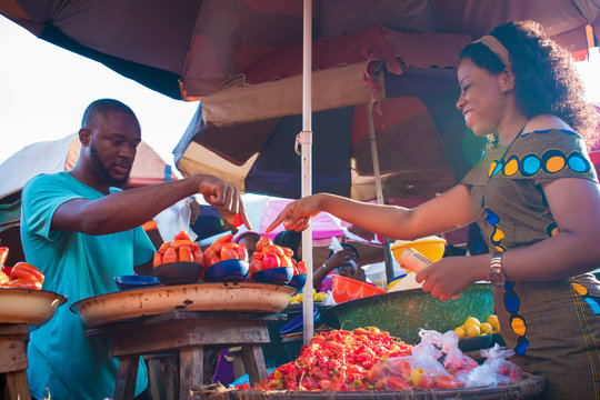 Black Girl Choosing Tomatoes From A Local Market Seller. Man Selling Tomatoes To A Young Woman