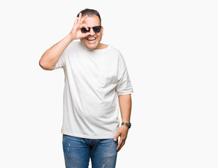 Fototapeta premium Middle age arab man wearig white t-shirt and sunglasses over isolated background doing ok gesture with hand smiling, eye looking through fingers with happy face.