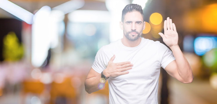 Handsome man wearing white t-shirt over night outdoors background Swearing with hand on chest and open palm, making a loyalty promise oath