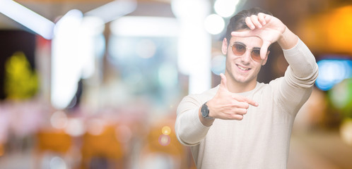 Fototapeta na wymiar Young handsome man wearing sunglasses over isolated background smiling making frame with hands and fingers with happy face. Creativity and photography concept.