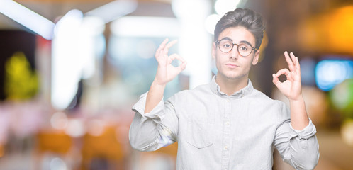 Young handsome man wearing glasses over isolated background relax and smiling with eyes closed doing meditation gesture with fingers. Yoga concept.