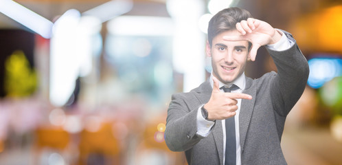 Young business man wearing suit and tie over isolated background smiling making frame with hands and fingers with happy face. Creativity and photography concept.